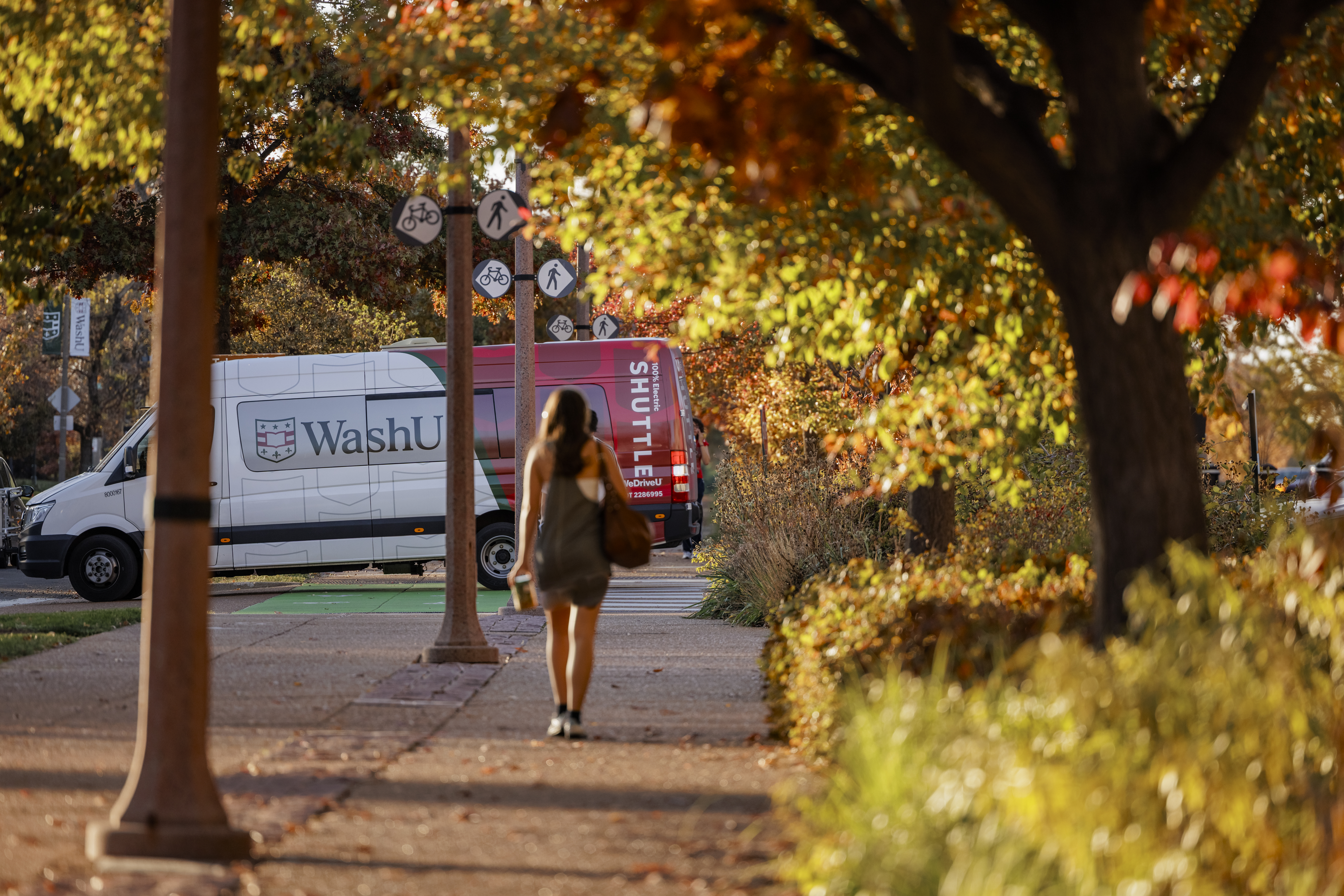 A WashU shuttle bus turns onto Forsyth Blvd. as pedestrians use the Centennial Greenway.
